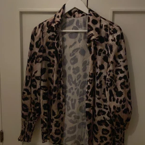 Leopardmönstrad skjorta i satin - Säljer en snygg leopardmönstrad skjorta i glansigt satinmaterial. Skjortan har långa ärmar med resår vid ärmsluten och klassisk krage. Perfekt för dig som vill sticka ut med ett djurmönster!