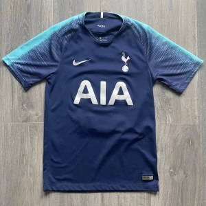 Tottenham fotbollströja  - Mörkblå Tottenham Hotspur fotbollströja från Nike med ljusblå ärmar och vitt tryck. Baksidan har Dempsey och nummer 2. Tillverkad i Dri-FIT material. 