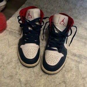 Nike Air Jordans blå, vita och röda - Säljer ett par Nike Air Jordans i blått, vitt och rött. Skorna har högt skaft, klassisk snörning och rund tå. Ikonisk Nike Swoosh på sidorna och röd insida. Perfekta för dig som gillar streetwear och sneakers med attityd.