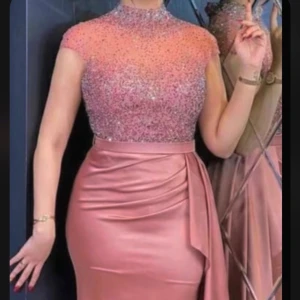 Glittrig långklänning i rosa med drapering - Säljer en elegant långklänning i skimrande rosa med glittrig överdel och hög hals. Klänningen har korta ärmar, figurnära passform och vacker drapering samt slits framtill. Storlek M & L 