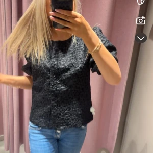Svart strukturerad blus - Säljer en svart blus med strukturerat tyg och korta ärmar. Blusen har en rak passform och rund halsringning. Perfekt att styla med jeans eller kjol för en trendig look.