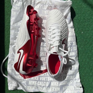 Nike fotbollsskor i vitt och rött - Säljer ett par Nike fotbollsskor i vitt med röda detaljer och metallicröd sula. Skorna har snörning och en rund tå, samt Nike-logga på skorna. Helt nya, aldrig använt dom. 