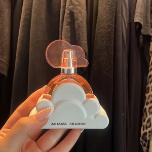 Ariana Grande Cloud Eau de Parfum 30 ml - Säljer en Ariana Grande Cloud parfym i en unik rund flaska med rosa detaljer och ett vitt molnformat stativ. Flaskan rymmer 30 ml och har en söt, feminin design med ett rosa molnlock. Perfekt för dig som gillar fruktiga och blommiga dofter.