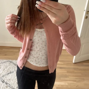 Ljusrosa kofta från H&M - Säljer en ljusrosa kofta från H&M i storlek XS. Koftan är stickad med ribbade muddar och knappar framtill. Perfekt att slänga över en topp för en söt och enkel look.