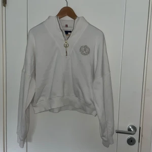 Vit ziptröja från Tommy Hilfiger - Säljer en vit långärmad ziptröja från Tommy Hilfiger med broderad logga på bröstet och dragkedja. Tröjan har en avslappnad passform och ribbade muddar. Perfekt för en stilren och sportig look.