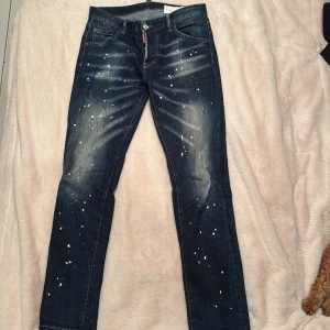 Mörkblå jeans med stänk och Canadian Icon-lapp - Dsquarde2 jeans i storlek 48, byxorna är i mycket bra skick endast använda ett få antal gånger. Inga byten mötts ej upp.