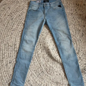 Ljusblå Replay Hyperflex Anbass jeans - Säljer ett par ljusblå Replay Hyperflex Anbass jeans med klassisk femficksdesign och snygga detaljer. Jeansen har normal/slim passform och är tillverkade i stretchigt denim för extra komfort. Perfekta för dig som gillar stilrena och bekväma jeans. (Andvända 2 ggr)