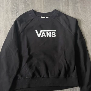 Svart sweatshirt från Vans - Säljer en svart sweatshirt från Vans med klassisk vit logga framtill. Tröjan har rund halsringning och långa ärmar med ribbade muddar vid ärmslut och nederkant. Använd endast en till två gånger!