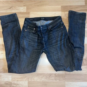 Svarta jeansbyxor från Jack & Jons  - Säljer ett par klassiska mörkblå jeans från Jack & Jons med fem fickor och raka ben. Jeansen har en snygg tvätt och detaljer i kopparfärgade nitar. Passar perfekt till vardags och har en tidlös look.