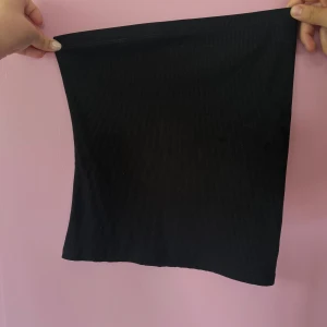 Svart ribbad tubtopp - En enkel svart ribbad tubtopp i stretchigt material. Perfekt att styla med jeans eller kjol för en clean look. Toppens raka form och avsaknad av axelband ger en minimalistisk känsla.