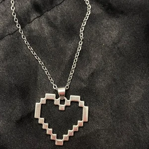Pixel Heart Halsband Pixelhjärta Silver Imitation - Så fint och unikt smycke som ser ut som ett pixel hjärta. Stilren design i silverimitation. Kedjan är justerbar 40-45 cm och hjärtat är ca 2 x 2,5 cm. Perfekt för den som älskar tv-spel