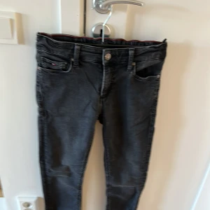 Svarta jeansbyxor från Tommy Hilfiger - Säljer ett par svarta jeansbyxor från Tommy Hilfiger med klassisk femficksdesign och diskret logga på fickan. Byxorna har normal passform och elastisk midja för extra komfort. Perfekta för dig som gillar stilrena och bekväma jeans. Slim Fit