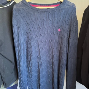 Marinblå kabelstickad tröja från Morris - Säljer en marinblå kabelstickad tröja från Morris med rund halsringning och diskret rosa logga på bröstet. Tröjan har långa ärmar och en snygg detalj med rosa insida vid halsen. Storleken är xxl men passar L/xl