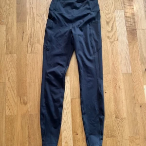 Svarta träningstights från hm move med fickor - Säljer ett par svarta träningstights från hm MOVE i storlek S. De har hög midja och praktiska fickor på sidorna, perfekta för mobilen. Materialet är stretchigt och bekvämt, passar perfekt till gymmet eller löprundan.