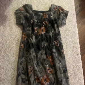 Blommig klänning från Nygårdsanna - Säljer en vacker blommig klänning från Nygårdsanna. Klänningen har korta ärmar och ett fint blommönster i orange och vitt på en mörk bas. Perfekt för en stilfull look.