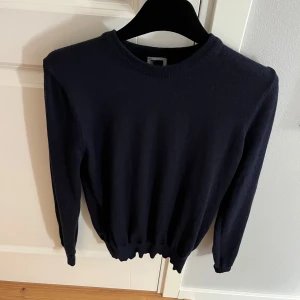 Mörkblå merino tröja - Säljer en stilren mörkblå stickad tröja med rund hals och långa ärmar. Perfekt för kyligare dagar och enkel att matcha med olika outfits. Tröjan har ribbade muddar vid ärmslut och nederkant för en bekväm passform. Storlek S men sitter som en XS.