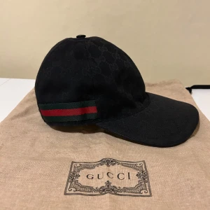 GUCCI Keps Svart - Säljer en snygg och äkta Gucci-keps i svart canvas. Klassisk design med justerbar rem baktill för perfekt passform. Diskret men lyxig med Gucci-logga framtill och högkvalitativa detaljer. Passar både vardag och fest – ett måste för den stilmedvetne! Följer även med orderbekräftelse  Skick: Mycket bra – sparsamt använd Storlek: S Färg: Svart Material: Canvas med läderdetaljer  Nypris: ca 5500kr Mitt pris: 1999kr  Skicka vid dm vid intresse eller för fler bilder! 