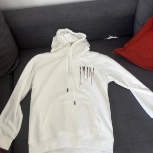 Vit hoodie från Amiri - Säljer en stilren vit hoodie från Amiri med färgglada detaljer och logotyp på både fram- och baksidan. Helt oanvänd med lapp på fortfarande! PRISET ÄR JUSTERBART