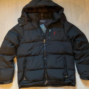 Svart Polo Ralph Lauren Puffer Jacket - Tja, säljer dennna sprillans nya Polo Ralph Lauren dun Jacka med lapp kvar i svart. Skicket är såklart 10 av 10 eftersom den är orörd. Jackan är i storleken S, säljer på grund av att den är för stor/inte jag på bilden. Ställ gärna frågor om ni undrar något😁 Pris kan diskuteras vid snabb affär!
