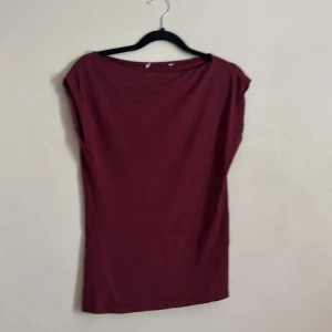 Vinröd topp - Säljer en stilren vinröd topp med korta ärmar. Perfekt för en avslappnad look eller att klä upp med accessoarer. Toppen har en enkel design som gör den lätt att matcha med olika outfits.