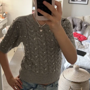 Grå stickad tröja med pärlor - Säljer en söt grå stickad tröja dekorerad med pärlor. Tröjan har korta ärmar och ett fint flätmönster. Perfekt för en stilren och mysig look. Säljer eftersom jag tycker jag inte passar i grå!❤️ superfint skick och använd typ 4 gånger!❤️