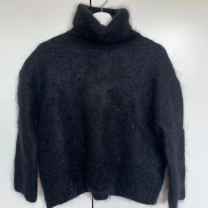 Svart ullig polotröja - Mysig svart polotröja med lång ärm och hög krage. Perfekt för kyliga dagar när du vill hålla dig varm och stilren. Tröjan har en mjuk och ullig textur som ger en lyxig känsla.