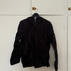 Stone Island Membrana 3LTC - Säljer en svart jacka från Stone Island med huva och dragkedja. Jackan har två fickor framtill med knappar. Solblekt fram till samt knapp som saknas på insidan, för övrigt i bra skick.