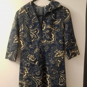 Klänning från 70talet  - Säljer en unik mönstrad klänning från Stockhaus i marinblått och beige. Klänningen har trekvartsärmar och ett iögonfallande paisleymönster samt fickor på sidorna. Klänningen har en krage och en dragkedja framtill.   Storlek uppskattas till 38, kanske mindre 40