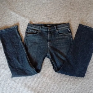 Mörkgrå jeans från Replay - Snygga mörkgrå jeans från Replay med klassisk femficksdesign och knappgylf. Perfekta för en avslappnad stil. Märkesdetaljer syns på bakfickan och linningen. Storlek 12-13 år
