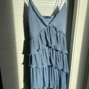Blå volangklänning från Zara - Säljer en snygg blå klänning från Zara med volanger och smala axelband. Perfekt för en somrig look. Klänningen har en v-ringad design och är tillverkad i ett lätt material som ger en luftig känsla.