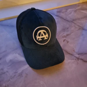 Grön keps med broderad logga - Snygg Grön keps med broderad logga framtill och texten 'All cap one' på sidan. Kepsen har ett nätmaterial baktill för extra ventilation och en justerbar rem för perfekt passform.