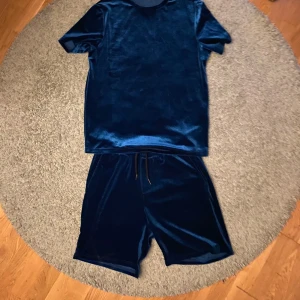 Blå sammetsset med t-shirt och shorts - Snyggt blått set i sammet med en t-shirt och matchande shorts. Perfekt för en avslappnad stil med en lyxig touch. Shortsen har snörning i midjan för justerbar passform.