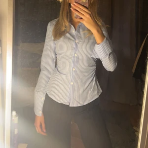 Blå och vit randig skjorta - Snygg blå och vit randig skjorta med långa ärmar och knappar framtill. Skjortan har en klassisk krage och en figurnära passform som ger en stilren look. Endast använd och tvättad en gång👌🏼👌🏼👌🏼👌🏼