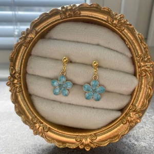 Blå blommiga örhängen - Handgjorda Charmiga örhängen med blå blommor och guldfärgade detaljer. Perfekta för att ge en färgklick till din outfit. Blommorna har en fin detalj i mitten som ger extra elegans.