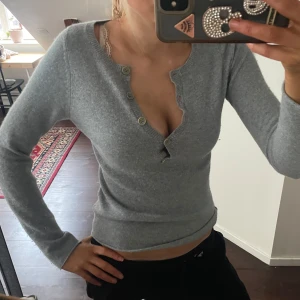 Grå/blå kashmirtröja från Zadig & Voltaire - Säljer en stilren grå kashmirtröja från Zadig & Voltaire med ett unikt tryck av en varg i turkos på framsidan. Tröjan har långa ärmar och knappar vid halsringningen för en snygg detalj.