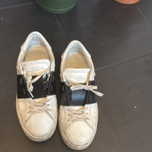 Valentino sneakers med svart detalj - Snygga Valentino sneakers i vitt med en bred svart rem över ovansidan. Skorna har ett helt okej skick med mycket kvar att ge. Pågrund av skicket är det ett billigare pris. Man får med sig box.