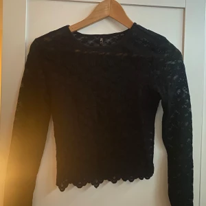 Svart spetsblus från ONLY - Snygg svart spetsblus från ONLY i storlek XS. Blusen har ett vackert spetsmönster och är långärmad med en croppad modell💕💕