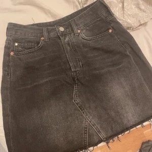 Svart jeanskjol - Snygg svart jeanskjol med klassisk femficksdesign och knappstängning. Kjolen har en rå kant nertill som ger en trendig look. Perfekt för en avslappnad stil.