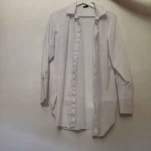Vit långärmad skjorta - Klassisk vit långärmad skjorta med krage och knappar. Perfekt för en stilren look. Passar både till vardag och mer formella tillfällen. Den är oversized.
