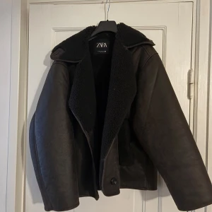 Brun läderjacka från Zara - Brun jacka från Zara med  fuskpälsfoder. Jackan har en bred krage och knappar framtill. Använd två gånger och är i nyskick 