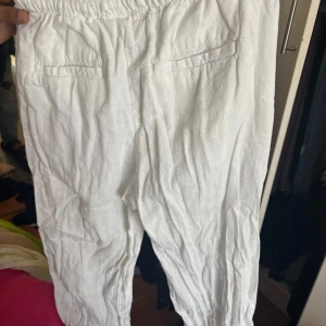 Vita linnebyxor - Säljer ett par vita linnebyxor med elastisk midja. Byxorna har en avslappnad passform och är perfekta för varma dagar. De har fickor baktill och är tillverkade i ett lätt och luftigt material. Köpt från Hm och Använd några gånger