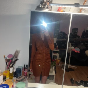 Glittrig brun klänning från Bik Bok - Snygg glittrig brun/kopparfärgad klänning från Bik Bok med lång ärm och knappar framtill. Den har en åtsittande passform och rynkdetaljer som ger en fin siluett. Perfekt för en kväll ute! Köpt till nyår men aldrig använd då jag valde en annan outfit istället. Inga defekter. 💕