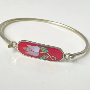 Silverarmband med röd emalj och blomdesign - Elegant vintage silverfärgat armband med en röd emaljdetalj som har en vacker blomdesign i vitt och grönt. Armbandet har en enkel och stilren design som passar perfekt som en subtil accessoar.