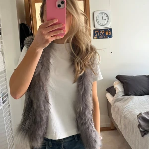 Grå pälsväst från Natures Collection - Säljer en snygg grå pälsväst från Natures Collection. Västen har en fluffig och mjuk textur som ger en lyxig känsla. Perfekt för att lägga till lite extra stil till din outfit. Passar bra till både jeans och klänning.