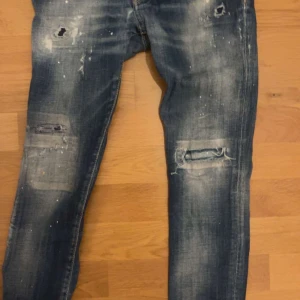 Blå slitna jeans - Säljer ett par blå jeans med slitningar och hål för en cool look. Jeansen har en skinny passform och är perfekta för en avslappnad stil. De har klassiska fem fickor och en dragkedja. Märke dsquared2