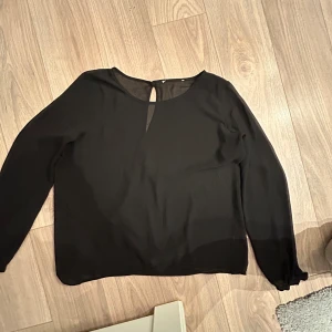 Svart blus med knappdetalj - Elegant svart blus med långärmad design och knappdetalj i nacken. Perfekt för en stilren look. Pris kan diskuteras