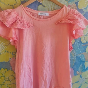 Rosa topp med spetsdetaljer från Tintoretto - Säljer en söt rosa topp från Tintoretto med spetsdetaljer på axlarna. Toppen har korta ärmar och en rund halsringning. Perfekt för en somrig look! 🌸