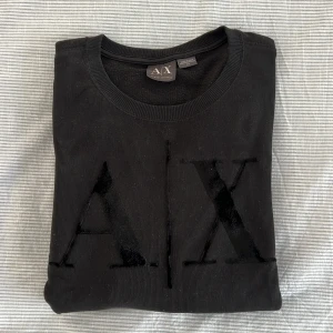Svart tröja från Armani Exchange - Snygg svart tröja från Armani Exchange med stort A|X tryck på framsidan. Tröjan har långa ärmar och rund halsringning. Perfekt för en stilren look.