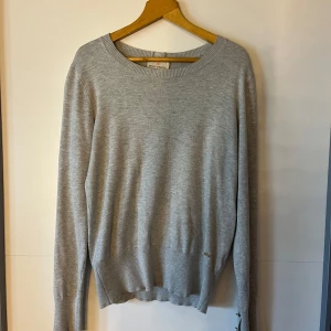Grå tröja från Holly & Whyte - Säljer en stilren grå tröja från Holly & Whyte by Lindex. Tröjan har långa ärmar och knappar på baksidan samt vid ärmsluten. Perfekt för en avslappnad look.