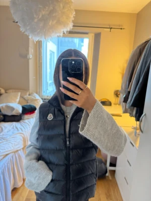 Svart dunväst från Moncler - Snygg svart dunväst från Moncler med hög krage och dragkedja framtill. Västen har ett quiltat mönster och den klassiska Moncler-loggan på bröstet. Perfekt att slänga över en hoodie eller stickad tröja för en chill och trendig look.